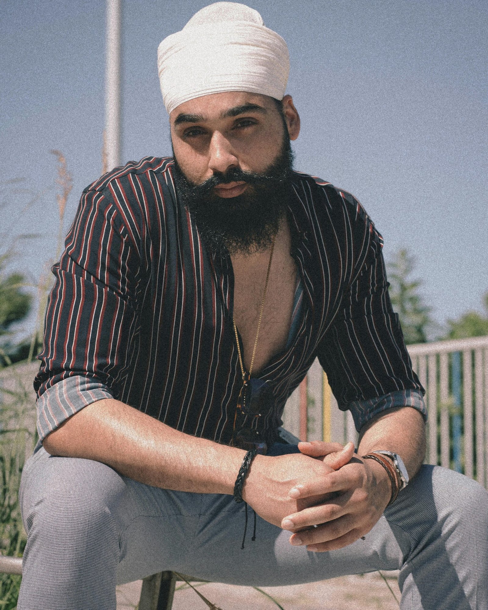 Portrait of a bearded man wearing a turban, seated outdoors on a sunny day.