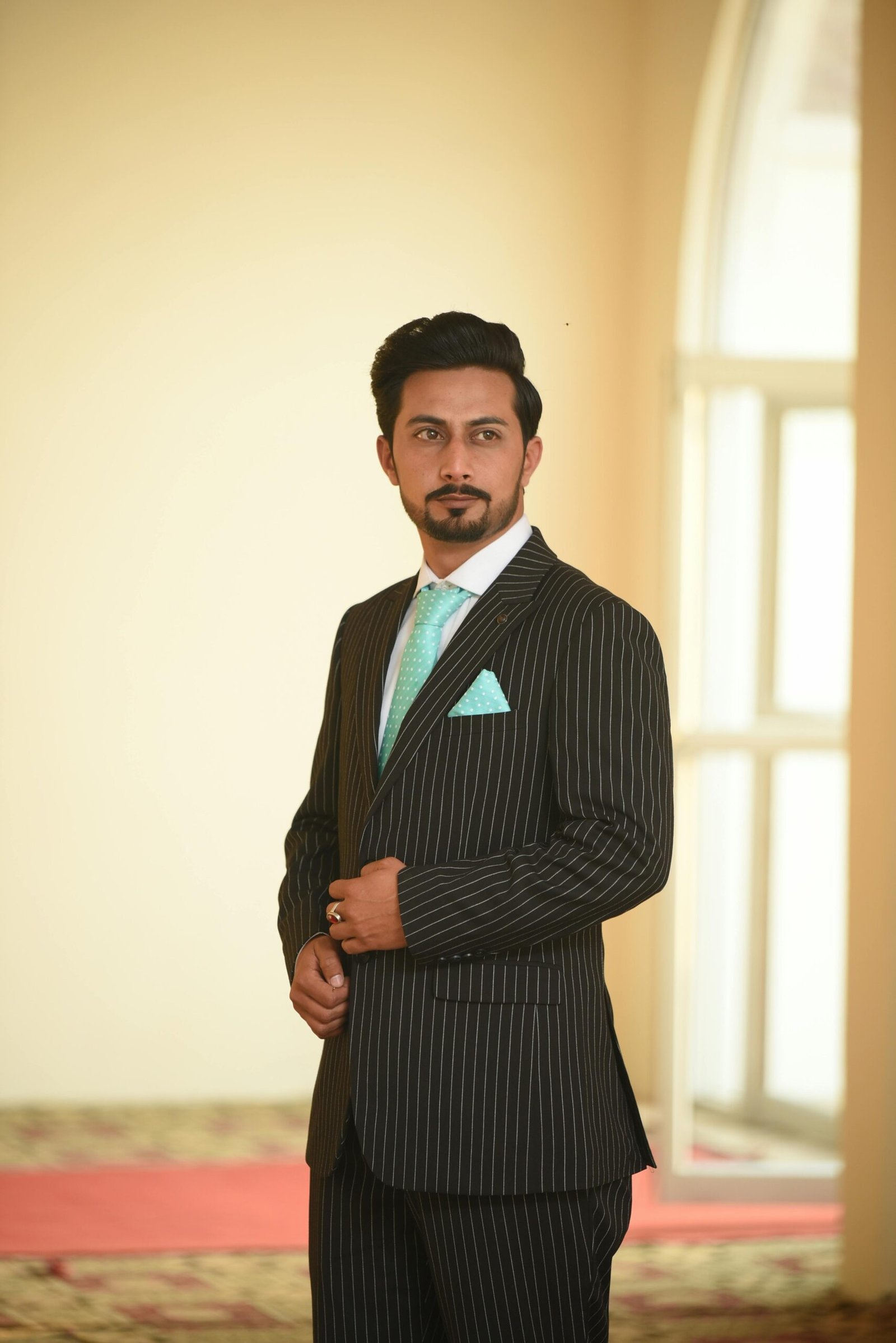 Portrait of a man in a pinstripe suit with a turquoise tie, indoors.